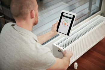 Ein Fachhandwerker hält ein Tablet in der Hand und führt einen hydraulischen Abgleich an einem Heizkörper durch
