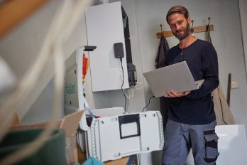 Ein Fachhandwerker wartet eine Gasheizung mit einem Laptop in der Hand