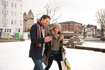 Ein junges Paar auf Shopping-Tour in einer verschneiten Stadt. In den Einkaufstaschen werden unter Umständen erhebliche Mengen an virtuellem Wasser nachhause getragen.