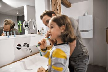 Vater und Tochter putzen sich die Zähne. Sie haben dabei den Wasserhahn abgedreht und sparen deshalb viel Wasser.