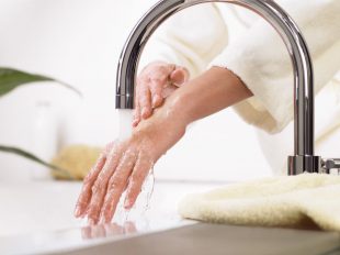 Eine Frau lässt aus dem Wasserhahn Wasser sanft über ihre Hand laufen. Trinkwasser ist spürbar lebenswichtig.