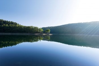 Sonnenstrahlen lassen die Wasseroberfläche einer Trinkwasser-Talsperre in verschiedenen Blautönen schillern.