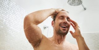 Ein Mann genießt eine warme Dusche. Das Wasser rieselt angenehm von oben herab.