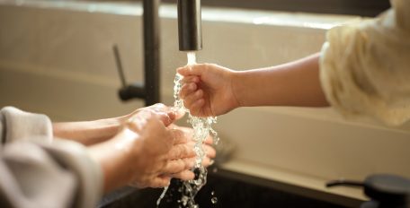 Laufender Wasserhahn mit Händen, die unter das Wasser gehalten werden