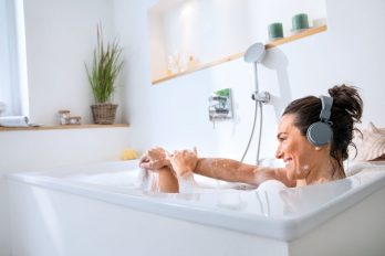 Eine Frau entspannt in der Badewanne und genießt über Kopfhörer Musik.