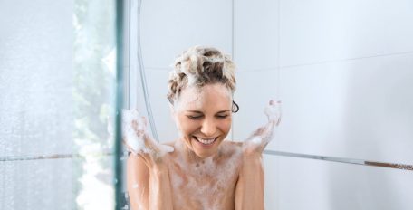 Eine Frau steht mit eingeschäumten Haaren unter der Dusche, aber das Wasser bleibt aus.