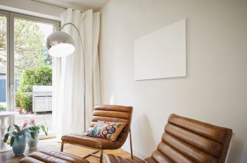 In einem Wohnzimmer scheint ein weißes Bild an der Wand zu hängen. Aber der Schein trügt. Es ist eine Elektroheizung: ein Infrarotheizkörper.