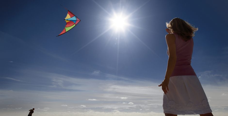 Extreme Hitze in Folge des Klimawandels: Eine Frau steht am Strand in der grellen Sonne und sieht beim Drachensteigen zu.