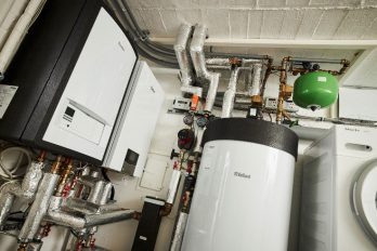 Blick in den kleinen Heizungskeller eines energetisch sanierten Altbaus, in dem neben einem Gas-Brennwertgerät auch die Inneneinheit einer Wärmepumpe an der Wand hängt.