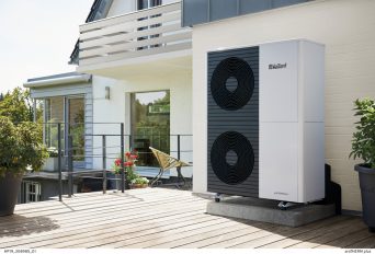 Eine moderne Wärmepumpe steht abseits der Terrasse eines älteren Einfamilienhauses.