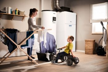 Eine Frau hängt im Hauswirtschaftraum Wäsche auf. Dabei unterhält sie sich mit ihrem kleinen Sohn. Im Hintergrund steht eine moderne Heizungsanlage.