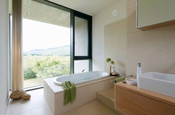 Das Bild zeigt ein modernes Badezimmer mit einem bodentiefen Fenster, durch das der Blick auf die weite Landschaft fällt.