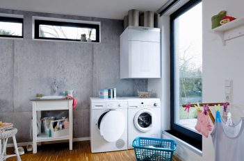 In einem Hauswirtschaftsraum hängt das zentrale Lüftungsgerät über der Waschmaschine.