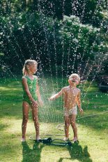 Zwei Kinder spielen mit einem Wassersprenger.