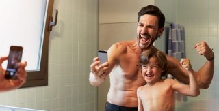 Vater und Sohn posieren vor dem Spiegel für ein Selfie.
