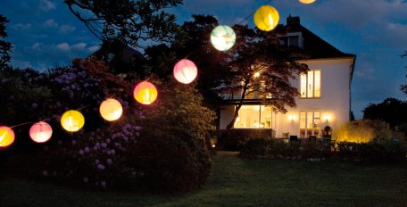 In der Abenddämmerung hängen Gartenlampions vor einem hell erleuchteten Einfamilienhaus.