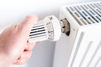Person, die am Thermostat eines Heizkörpers dreht