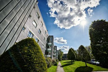 Strahlend blauer Himmel und Sonne über einem Mehrfamilienhaus mit einer großen Grünfläche davor.