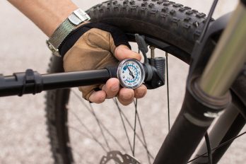 Mit einer Fahrradpumpe mit Druckanzeige pumpt jemand den Reifen des Fahrrads auf.