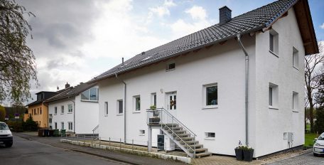 Unter der Treppe zur Haustür eines älteren Einfamilienhauses steht eine Luft/Wasser-Wärmepumpe.