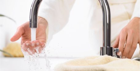 Eine Person prüft mit der Hand am Waschbecken die Temperatur des einlaufenden Wassers.