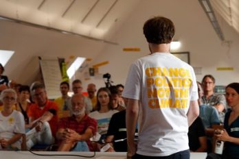 Ein Mann hält vor Bürgern und Bürgerinnen einen Vortrag. Auf seinem T-Shirt steht "Change politics not the climate"