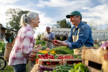 Glücklicher Landwirt, der auf einem Bauernmarkt Erdbeeren an eine Kundin verkauft