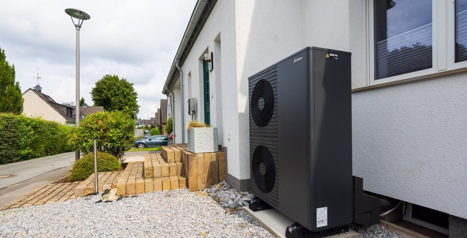 Vor einem sanierten Einfamilienhaus steht eine neue Luft/Wasser-Wärmepumpe aroTHERM plus