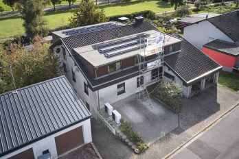 Vogelperspektive eines mit einer PV-Anlage bedeckten Zweifamilienhauses, dazu zwei Luftwärmepumpen