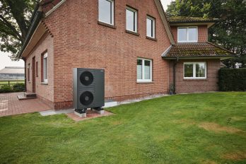 Das Bild zeigt einen verklinkerten Altbau im Münsterland aus den 50er-Jahren mit einer Wärmepumpe vor der Hauswand