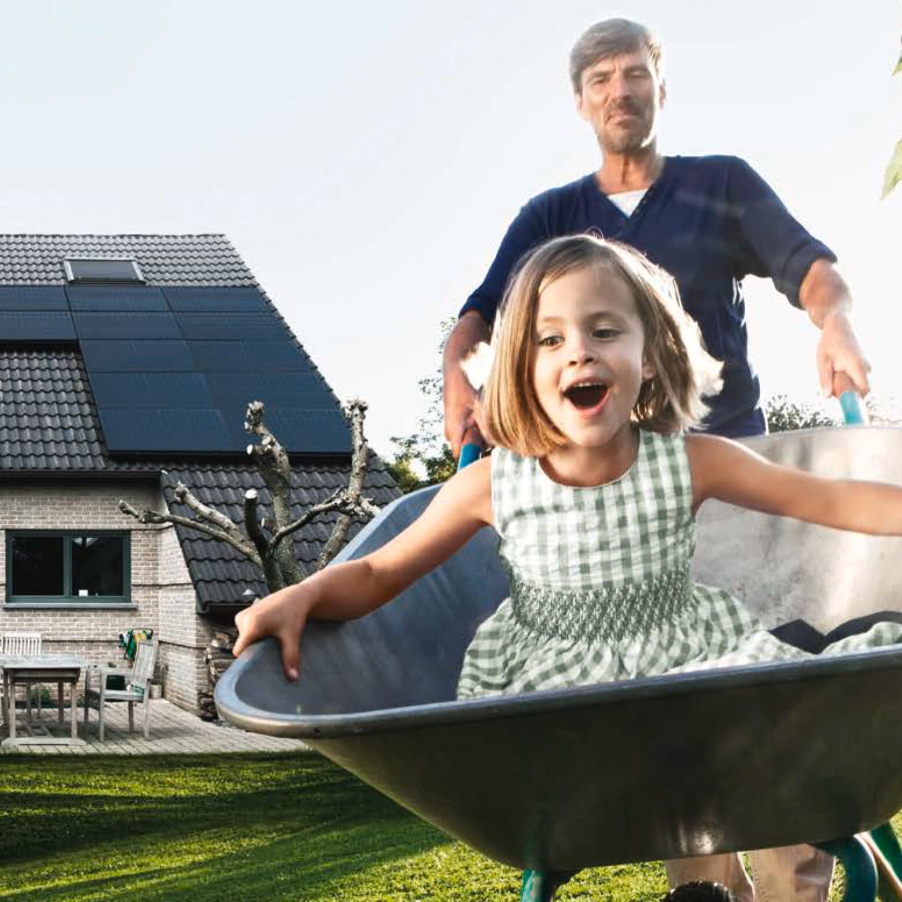 Ein Mann fährt ein Kind in einer Schubkarre durch den Garten.