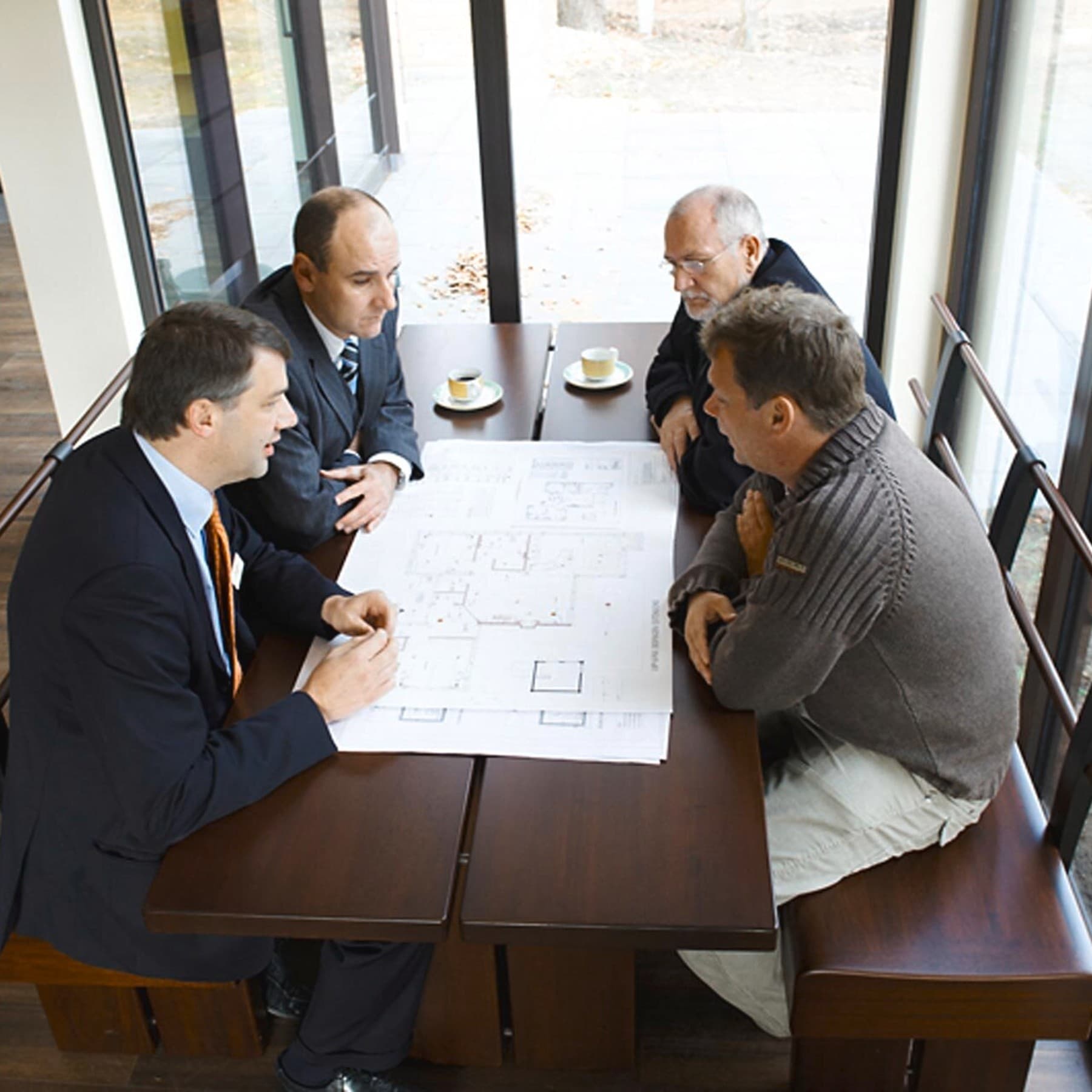 Lutz Pumpa sitzt mit drei anderen Leuten an einem Tisch und schaut gemeinsam mit ihnen in einen Bauplan