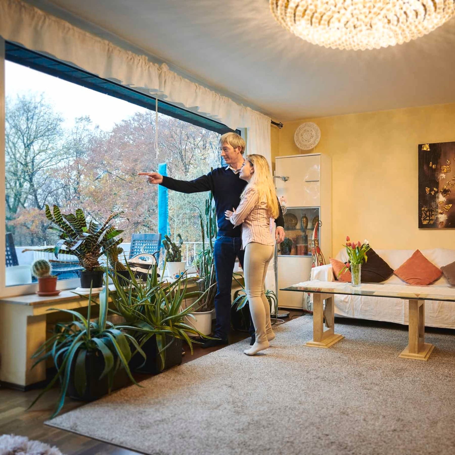 Ehepaar steht an großer Fensterfront im Wohnzimmer und schaut nach draußen