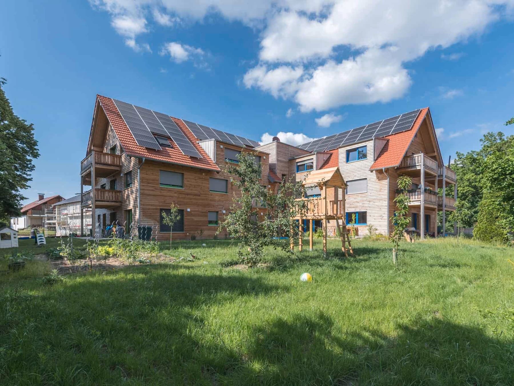 Blick auf ein großes Mehrfamilienhaus aus Holz, auf dem eine große Solaranlage installiert ist