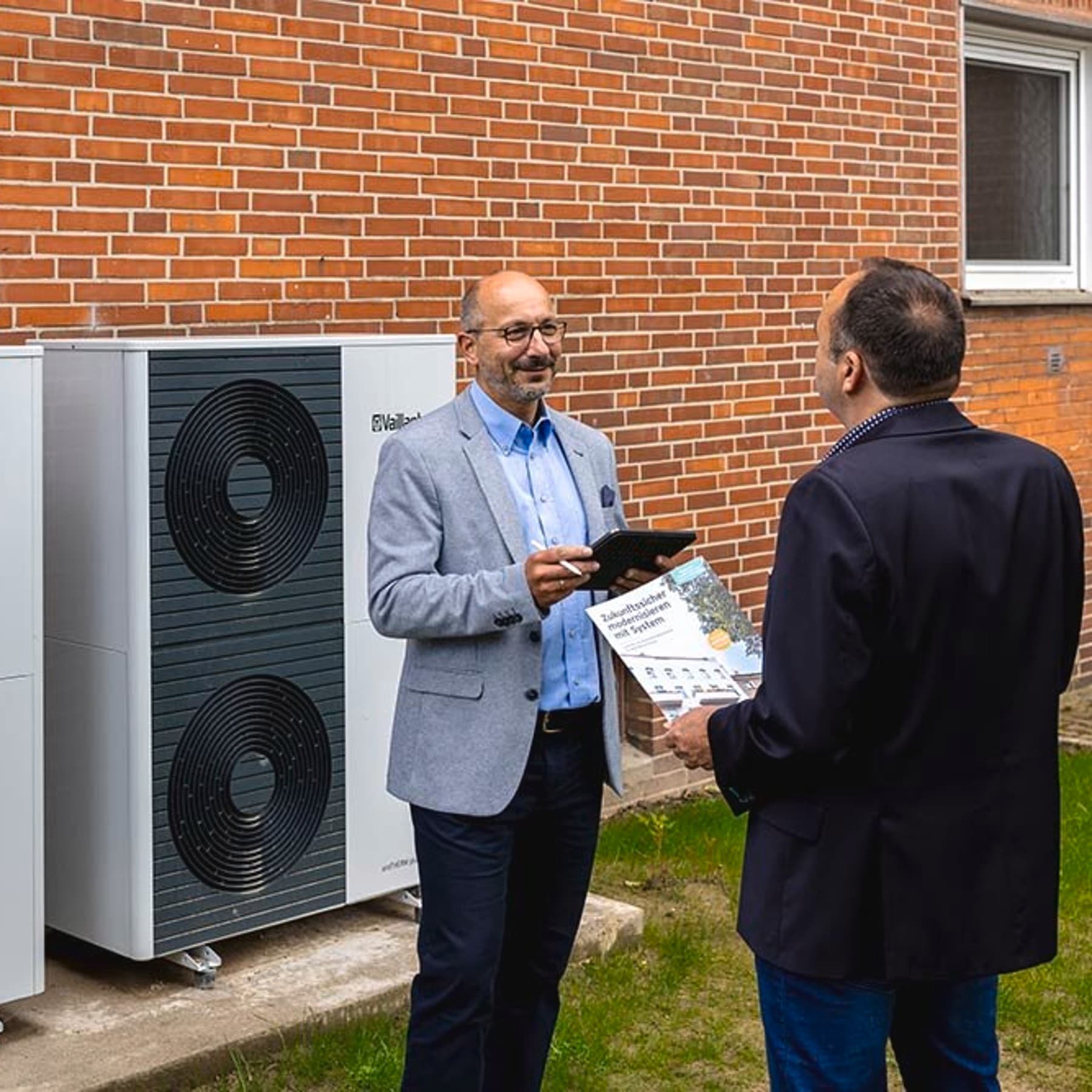 Zwei Personen stehen draußen neben den Wärmepumpen Außeneinheiten