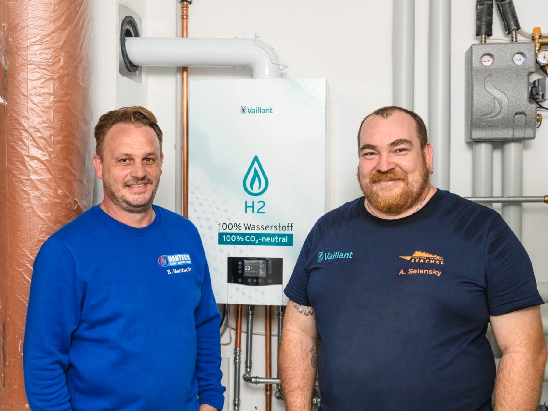 Zwei Fachhandwerker stehen vor einem „100% H2-Brennwertgerät“ von Vaillant im Heizungsraum