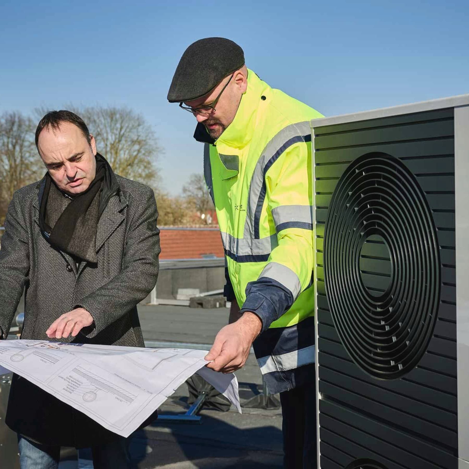 Zwei Personen stehen mit einem Bauplan neben der Wärmepumpe