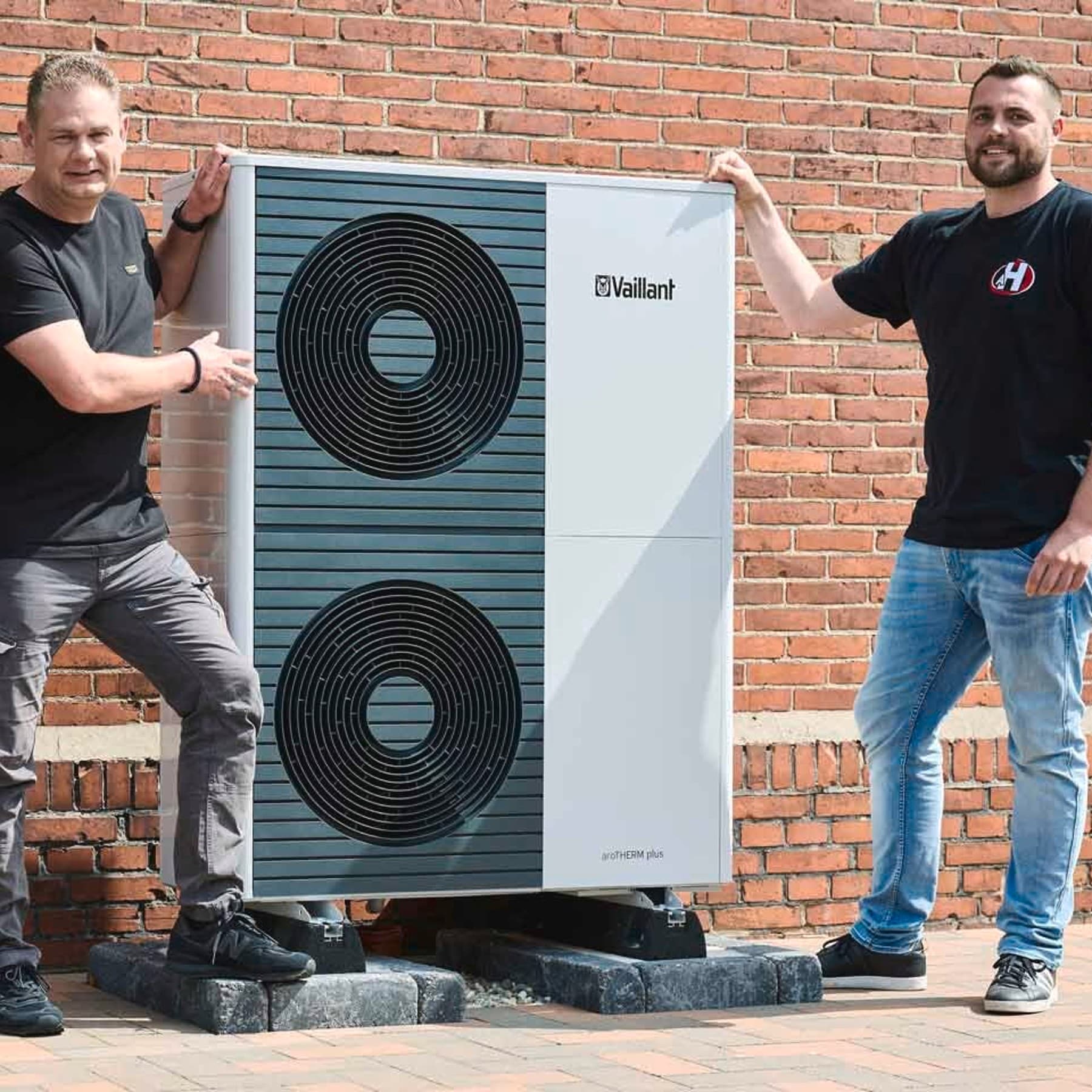 Heizungsbauer und Hausbesitzer stehen neben der Wärmepumpen Außeneinheit
