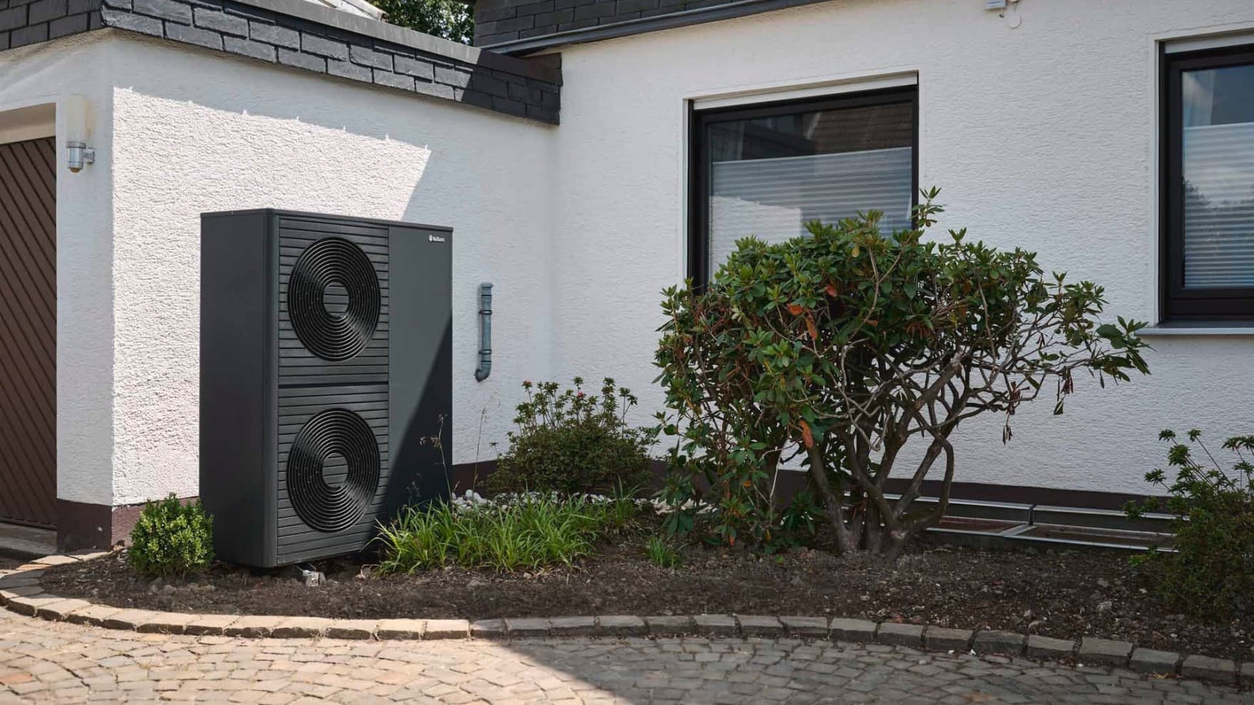 Doppelstöckige Wärmepumpe aroTHERM plus im Vorgarten vor weißer Hauswand