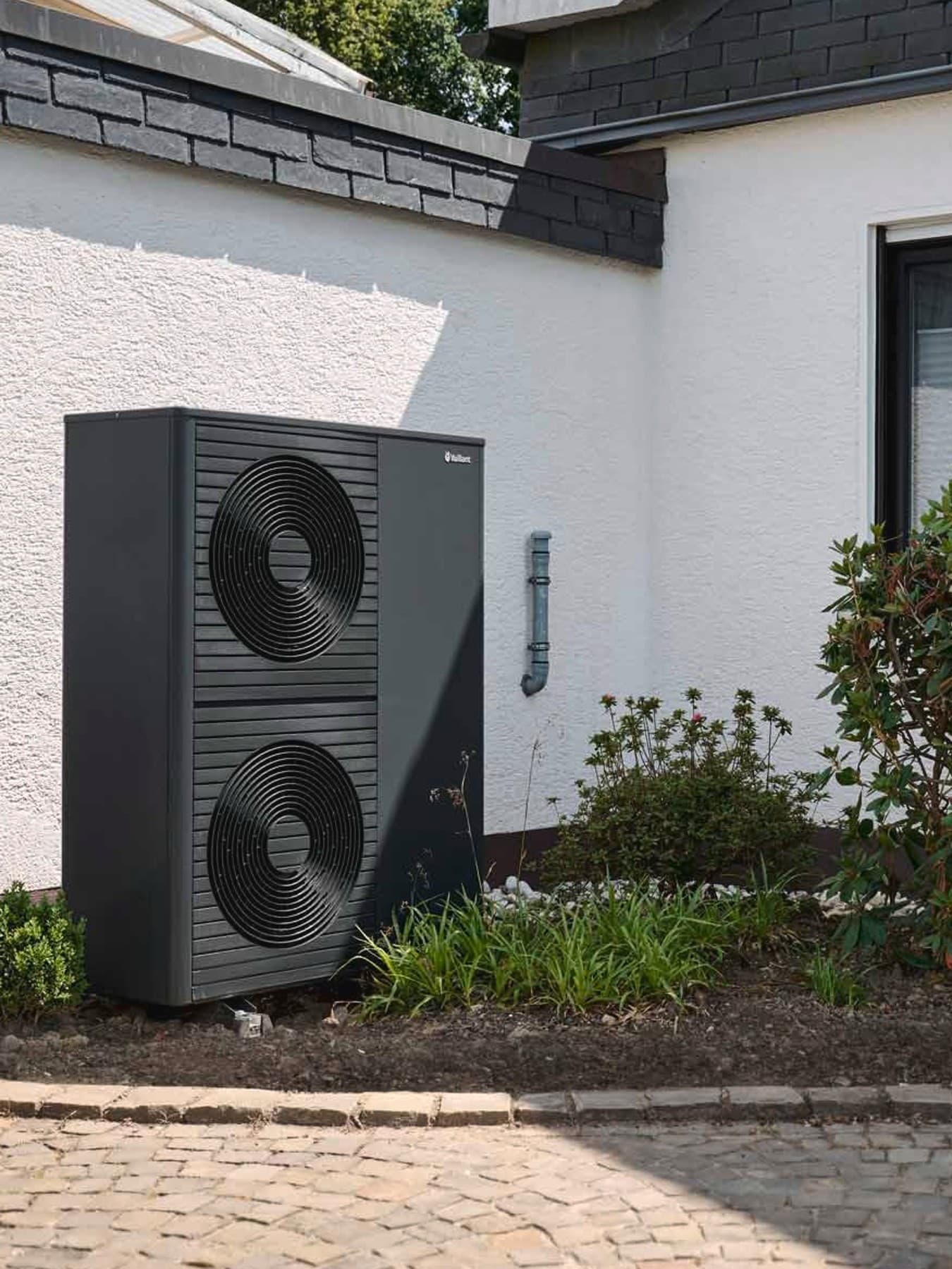 Doppelstöckige Wärmepumpe aroTHERM plus im Vorgarten vor weißer Hauswand