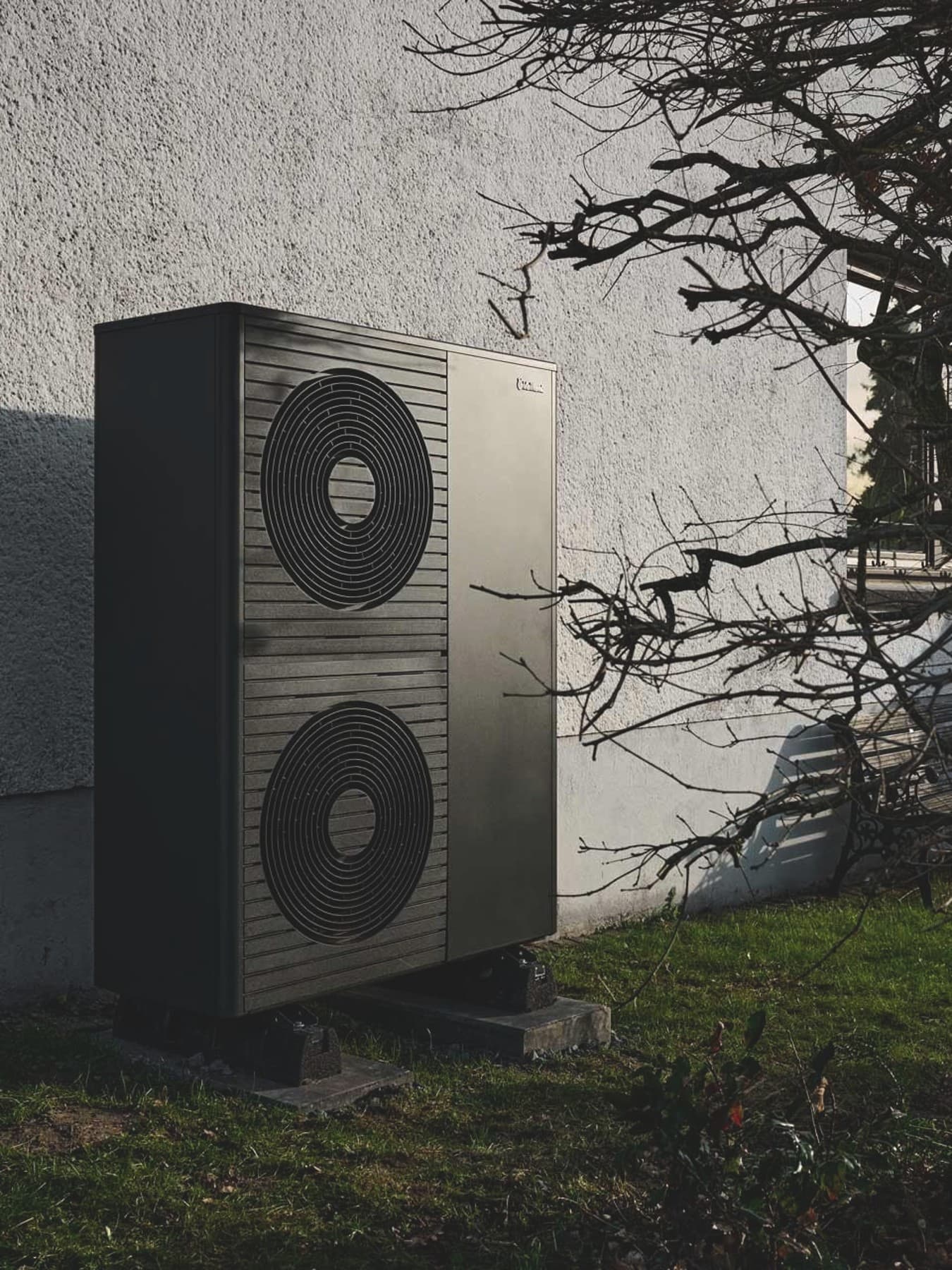 : Außeneinheit einer Wärmepumpe von Vaillant an der Hauswand eines verputzten Wohngebäudes. Die rechteckige, dunkelgraue Wärmepumpe aroTHERM plus mit zwei