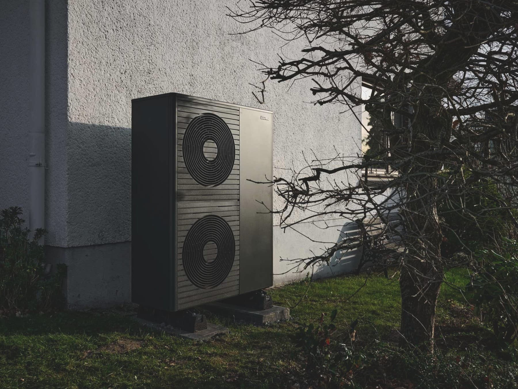 : Außeneinheit einer Wärmepumpe von Vaillant an der Hauswand eines verputzten Wohngebäudes. Die rechteckige, dunkelgraue Wärmepumpe aroTHERM plus mit zwei