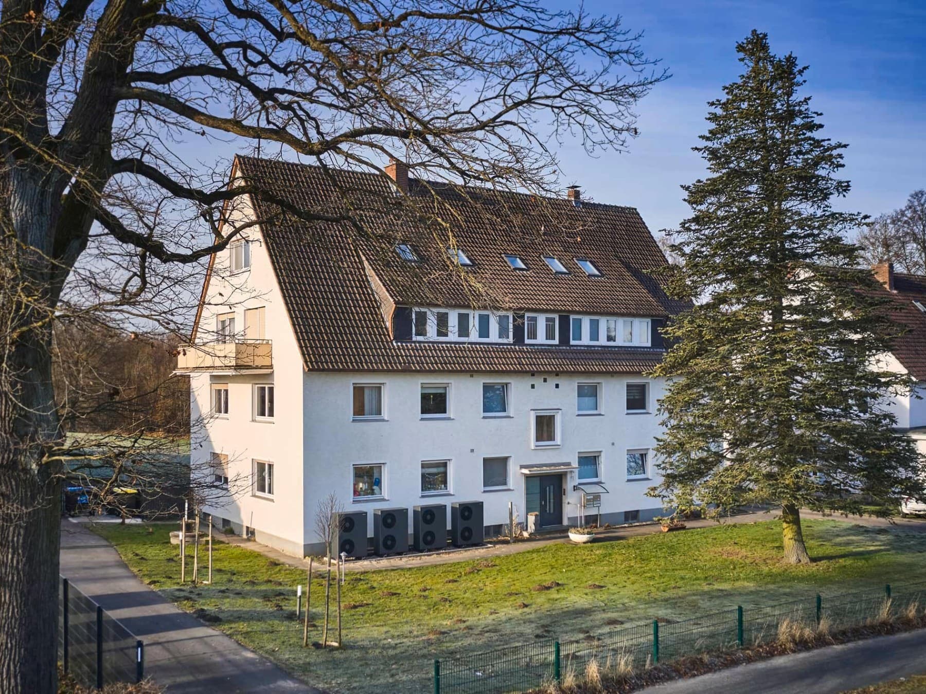 Außenansicht eines Mehrfamilienhauses mit mehreren entlang der Fassade installierten Luft/Wasser-Wärmepumpen vom Typ aroTHERM plus von Vaillant und umliegender Grünfläche.