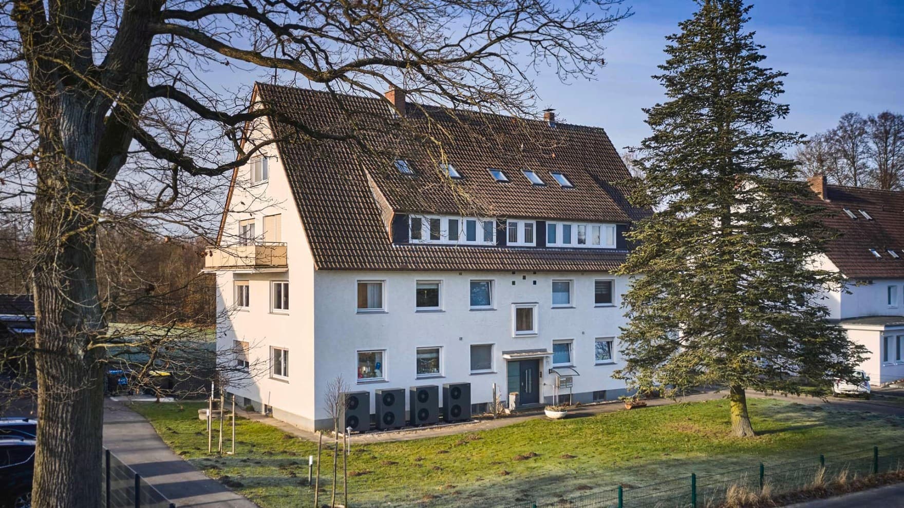 Außenansicht eines Mehrfamilienhauses mit mehreren entlang der Fassade installierten Luft/Wasser-Wärmepumpen vom Typ aroTHERM plus von Vaillant und umliegender Grünfläche