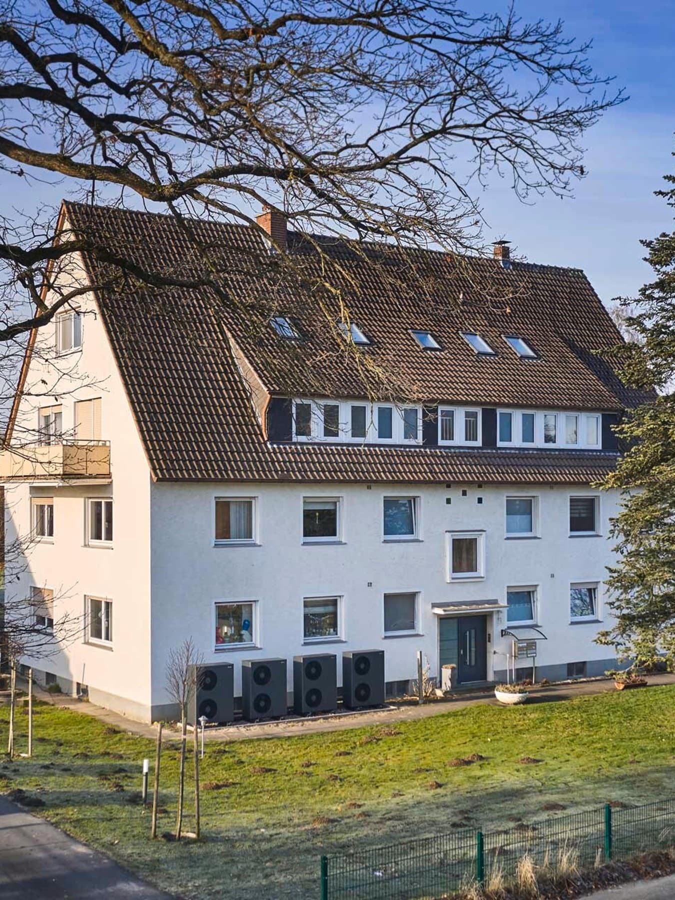 Außenansicht eines Mehrfamilienhauses mit mehreren entlang der Fassade installierten Luft/Wasser-Wärmepumpen vom Typ aroTHERM plus von Vaillant und umliegender Grünfläche