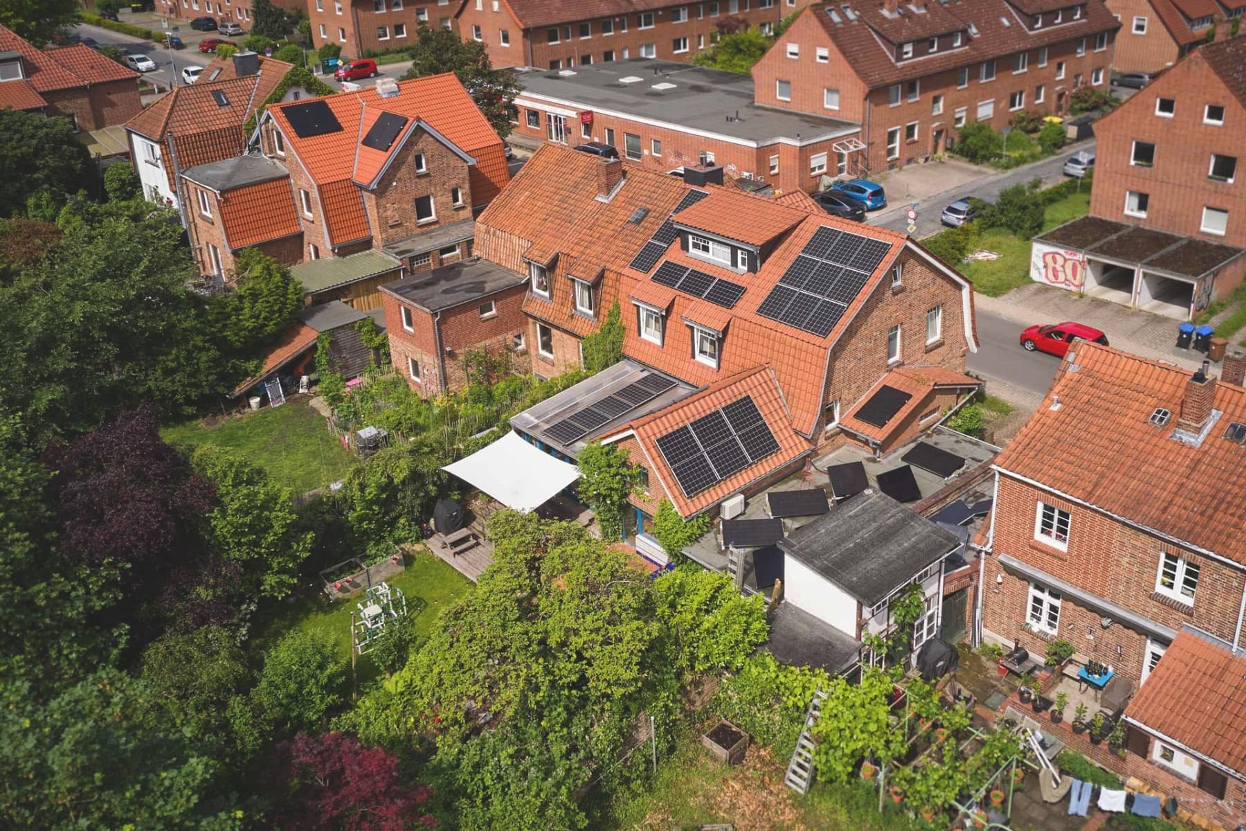 Straßenzug mit mehreren Wohnhäusern, eines davon mit großflächig installierten Photovoltaikmodulen auf dem Dach.