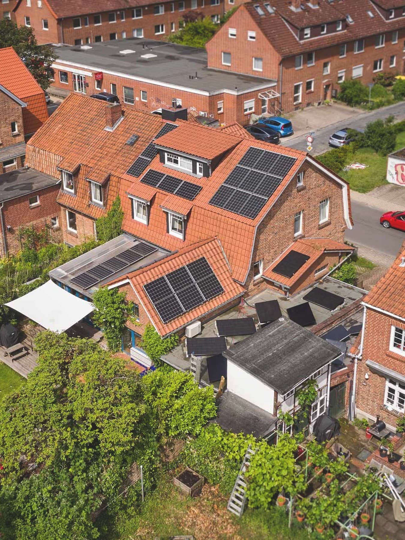 Straßenzug mit mehreren Wohnhäusern, eines davon mit großflächig installierten Photovoltaikmodulen auf dem Dach.