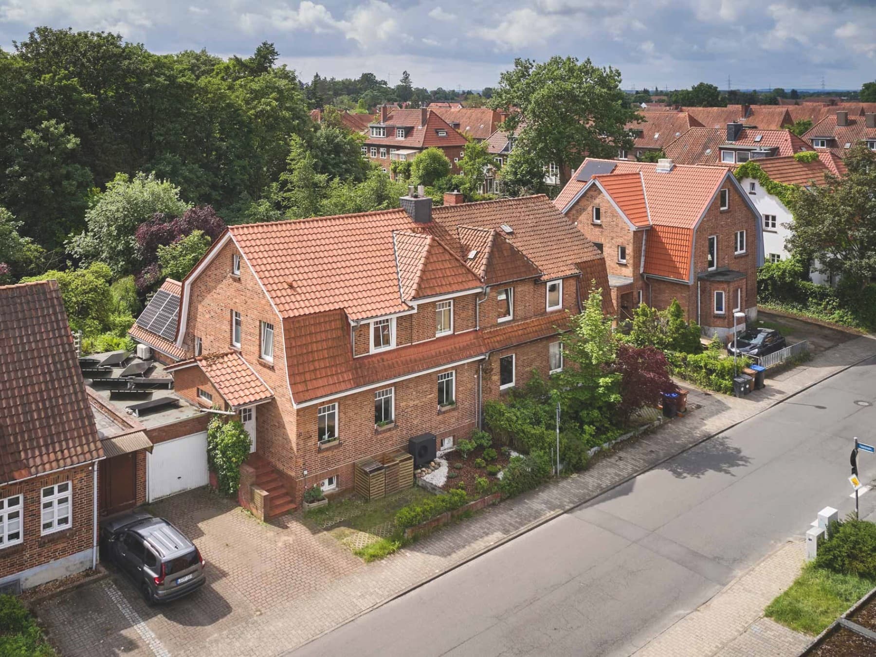 Luftaufnahme eines Backstein-Doppelhauses in einer Wohnstraße mit roten Ziegeldächern und sichtbarer Außeneinheit der Luft-Wasser-Wärmepumpe aroTHERM plus VWL 75/8.1 A von Vaillant an der Fassade.
