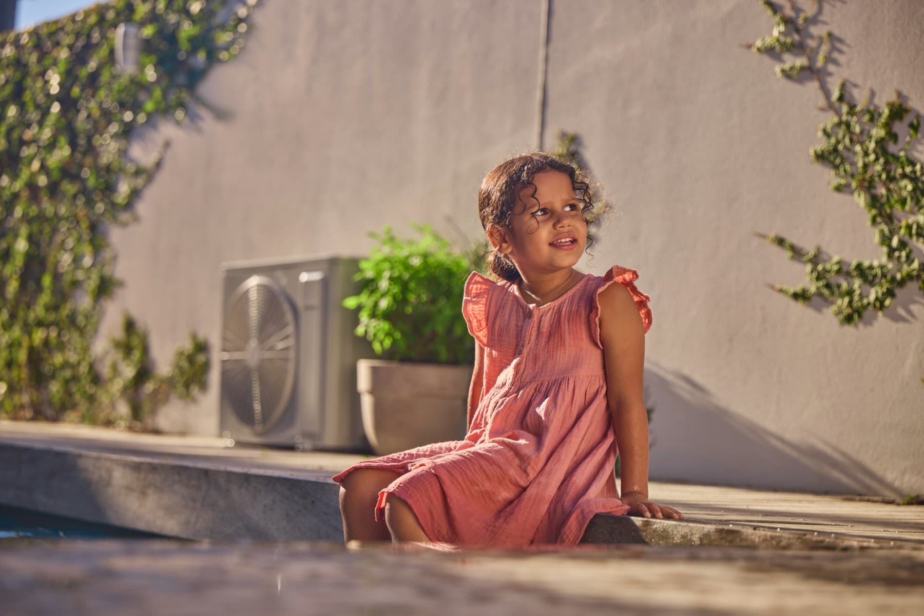 Kind auf einer Mauer sitzend mit einer Klimaanlage im Hintergrund