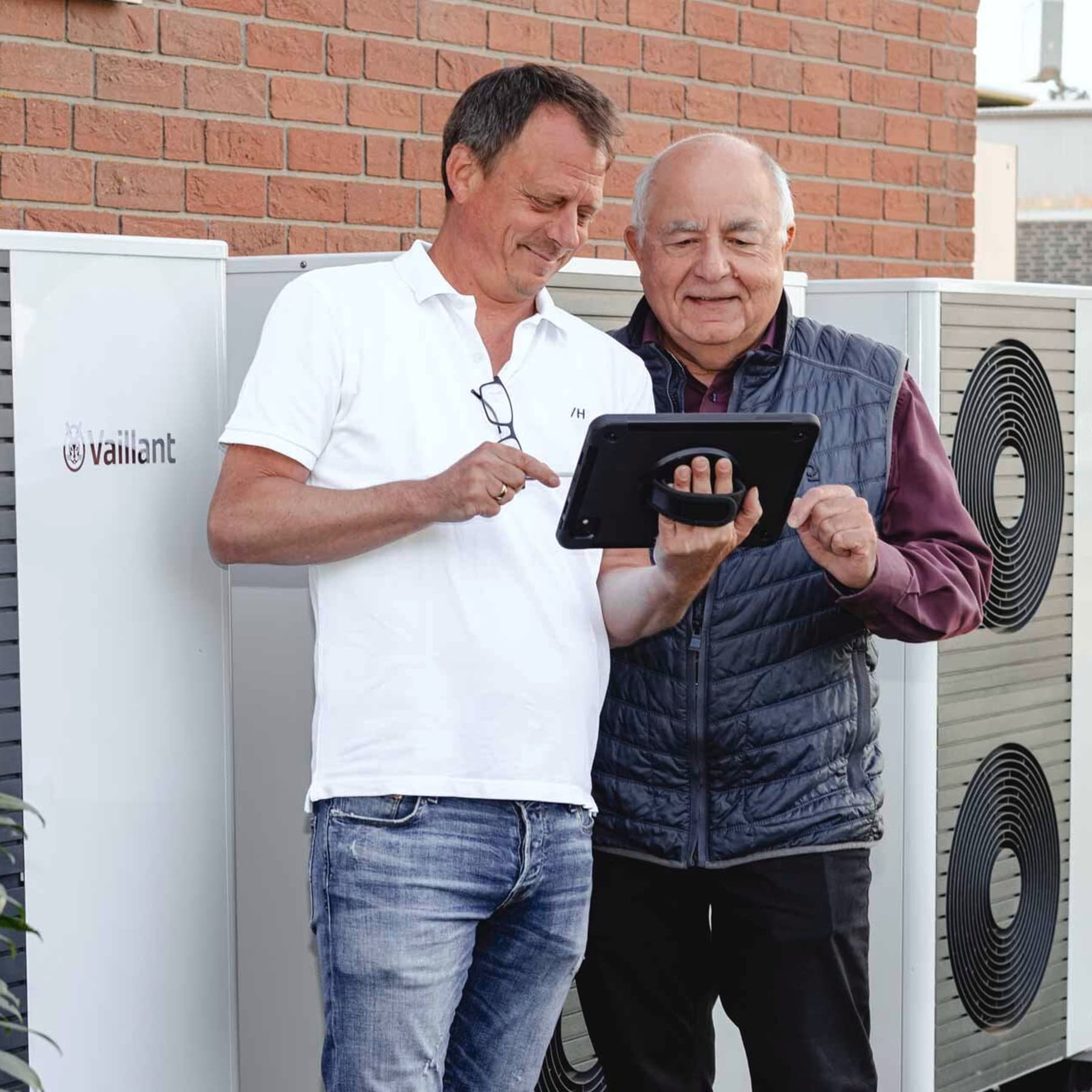 Zwei Männer an einem Tablet vor den Wärmepumpen Außeneinheiten